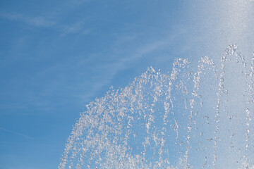 Water fountain spraying jets of sparkling water in lighlt clouded afternoon sky.