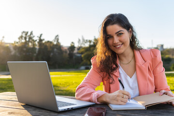 Businesswoman writing her notes in her notebook with her computer.