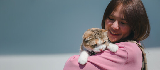 Young attractive Asian woman holding a cat with smiley face standing outdoor in the morning light sun beam. Pets makes people happy and relief the stress. Lovely kitty with girl.