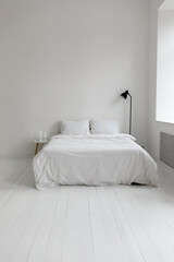 Fototapeta na wymiar Concept of interior design in white modern apartment. Cozy bedroom with home decor, houseplant, side table furniture and floor lamp near bed with cotton bedding. Morning in hotel, copy space
