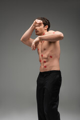 Fototapeta na wymiar man in black pants with red lip prints on shirtless torso obscuring face while posing on grey background.