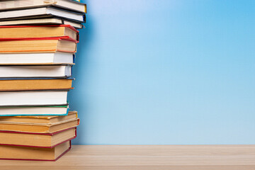 Stack of books in the colored cover lay on the wooden  table and blue backround. Education learning concept