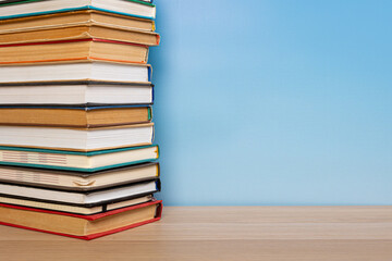 Stack of books in the colored cover lay on the wooden  table and blue backround. Education learning concept
