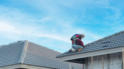 Workers are installing gray roof tiles wearing seat belts to ensure safe working at heights.