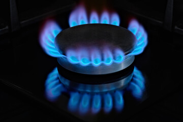 Burning kitchen gas burner with blue flame on cooking surface, natural gas economy concept