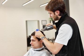 Fototapeta premium Professional hairdresser during work with man client with hair dryer