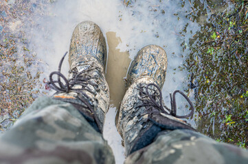 Close-up for a man's legs in military camouflage with a trekking wellington shoes dirty in mud