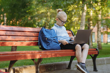 Fototapeta premium cute caucasian boy sitting on bench in park with laptop computer. Black screen