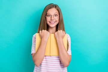 Photo of cheerful smart girl toothy smile arms hold hug book isolated on turquoise color background