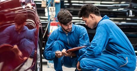 Obraz premium Automotive mechanic men checking at car tyre rubber condition needed for replacement, man pointing hand at wheel following maintenance checklist document, after service at auto repair shop concept