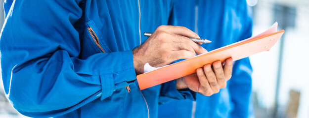 Automotive mechanic man checking damage part under car condition, vehicle maintenance technician write on checklist document in garage at auto repair shop on lifter hoist. after service