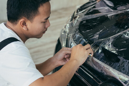 Asian detailing film paint protection men specialist cutting and wrapping car in garage showroom, protective coating installation and polishing automobile for vehicle care service business concept