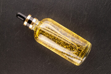 Face serum in glass bottle on slate stone, macro, top view.