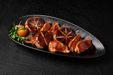 Appetizing fried shiitake mushrooms and slices on black plate of baked duck breast on black