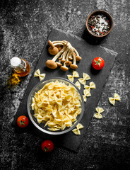 Raw Farfalle pasta in a bowl with mushrooms and tomatoes.