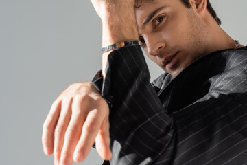 fashionable man in black blazer and silver bracelet looking at camera on blurred foreground...