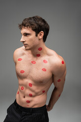Naklejka premium brunette man with red kiss prints on shirtless torso looking away on grey background.
