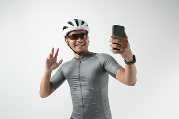 Photo of a young Asian man using a smartphone for a video call with family. Standing and isolated in a studio wearing a white bike helmet, Happiness on his face.