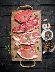 Raw meat. Pork and beef steaks on a tray with spices and rosemary sprig.
