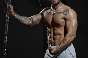Cropped image of sportive relief male body posing with sport gym equipment over dark background. Model posing shirtless. Concept of sport, workout, strength