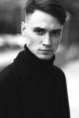 Fashion portrait of a young guy in black clothes of model appearance on the street among skyscrapers and alleys