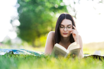 Beautiful girl lying in a park with a book. Outdoor leisure activity on a sunny summer day.