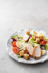 Caesar salad. Healthy salad made with chicken fillet, cherry tomatoes, iceberg lettuce, parmesan cheese and croutons on light grey background with copy space. Light diet dinner, text space
