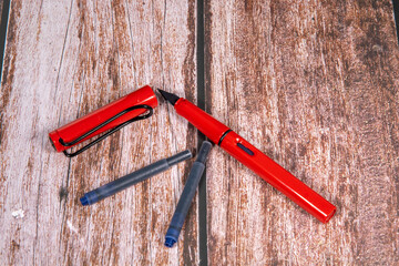 red fountain pen with nib and spare cartridges on a wooden base. Text space above.