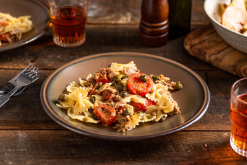 Farfalle pasta with tuna, tomatoes, kapers and oregano. Dark woode background. 