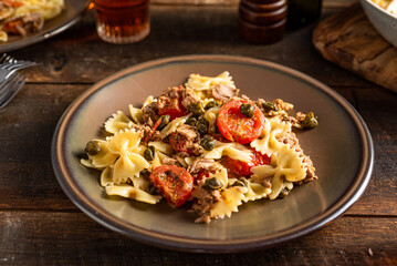 Farfalle pasta with tuna, tomatoes, kapers and oregano. Dark woode background. 