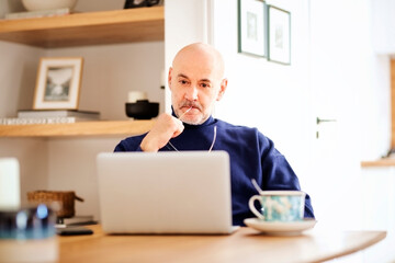  Businessman looking thoughtfully and using laptop while working from home