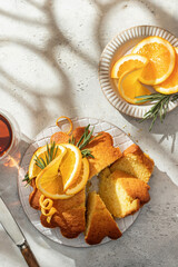 Sliced orange cake decorated with fresh orange slices on ceramic on light gray textured background, sunny morning breakfast in harsh light. Text space, flat lay, top view