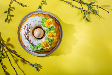 Easter cake decorated with icing and spring flowers with Easter eggs and willow twigs on yellow background. Happy easter holiday.