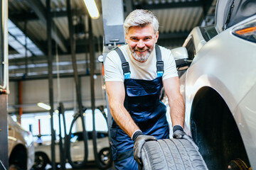 Beard handsome grey haired mature mechanic hold wheel automobile vehicle parts examining using...