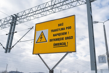 Warning sign with text in Polish language, means overhead electrical contact power lines, danger of...