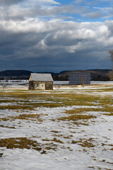 Fototapeta na wymiar One room log cabin shack with solar panel in farmers field with snow and clouds in winter