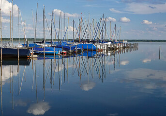 Row of small sailing boats moored at pier with reflection in water