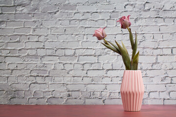 Pink Tulips in Vase on Pink Table Behind a brick Wall