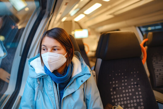 Asian Woman In Blue Jacket And Protective Mask Looking Out Of Train Window In Winter Day. Lifestyle Concept.