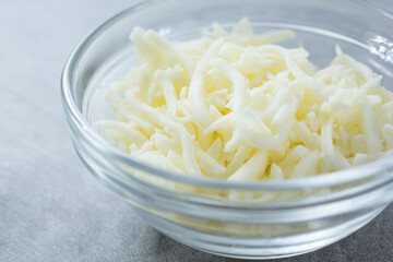 A closeup view of a glass condiment cup of shredded mozzarella cheese.