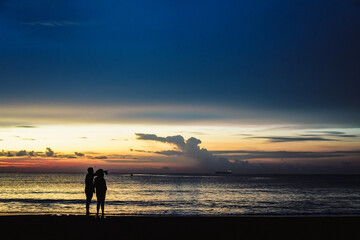 Young couple pointing away at seashore on summer evening. Silhouettes of man and woman on the beach