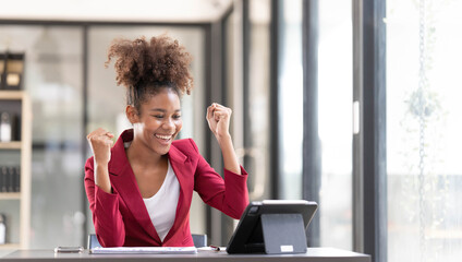 excited young lady worker sit by desk raise hands up after successful finish hard work on business...