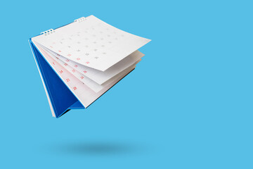 White paper desk calendar flipping page isolated on blue background - obrazy, fototapety, plakaty