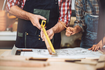 Small business furniture owner and professional architect interior designer working together in carpenter workshop with blueprint and tablet discussing about home furnishing design project.