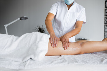 Obraz na płótnie Canvas Crop masseur applying scrub on leg of client in salon