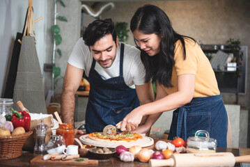 Young couple family caucasian man and asian women wearing aprons enjoy making pizza at home...