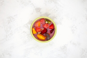 Sop Buah or Es Campur in green bowl on the table, top view. Es buah Indonesian popular fruit ice with grass jelly, syrup and milk. Mixed fruit cocktail