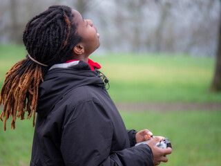 Young african girl standing flying drone outdoors in a park in cold weather.