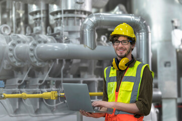 Inside the factory, a confident male engineer inspects the job with a laptop