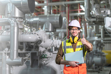 A male engineer in a portrait holding a laptop while a show thump up inside a factory.